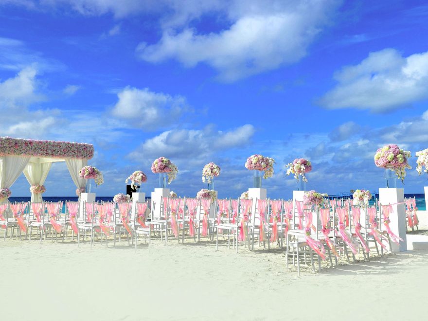 Flower arch and wedding chairs decorated in pink and white ribbons on beach