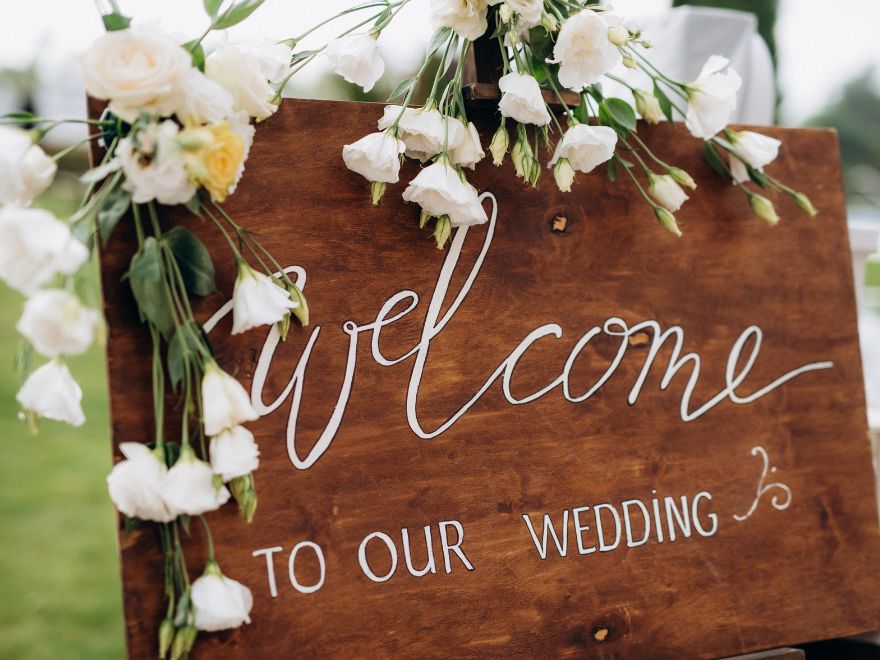 Wooden welcome to our wedding sign draped in white and yellow flowers